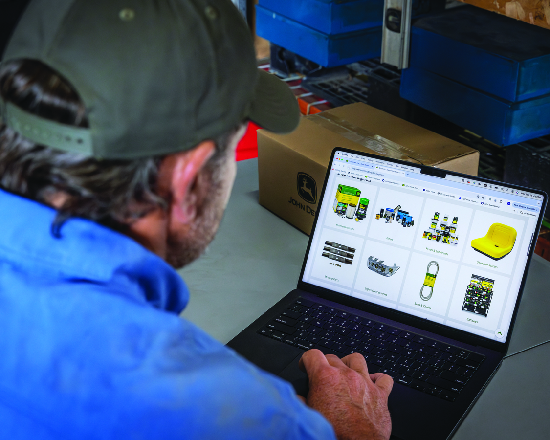 A person wearing a green baseball cap and a blue shirt is seen from behind, looking at a laptop scre